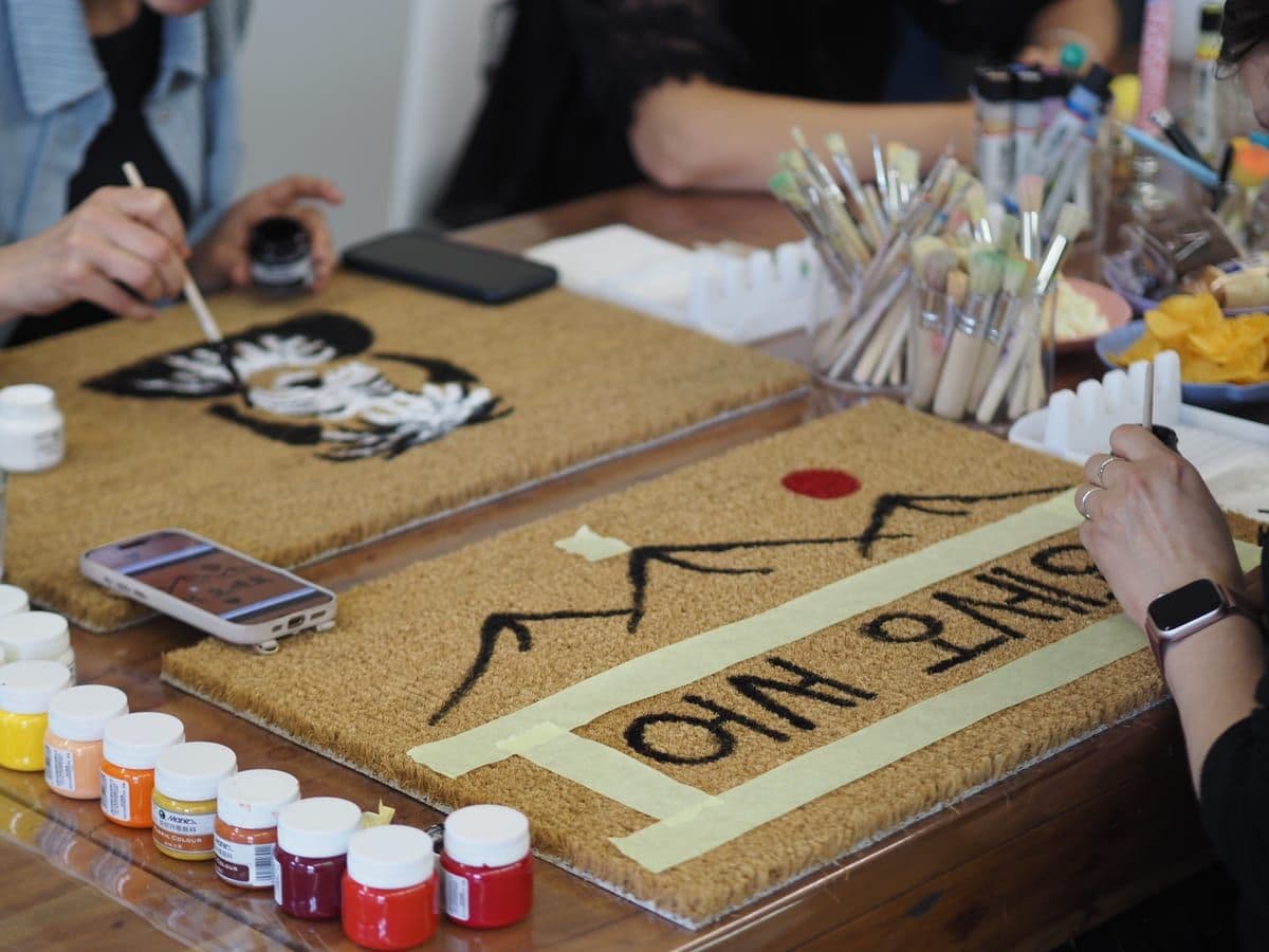 Two coir doormats being hand-painted at the studio table.