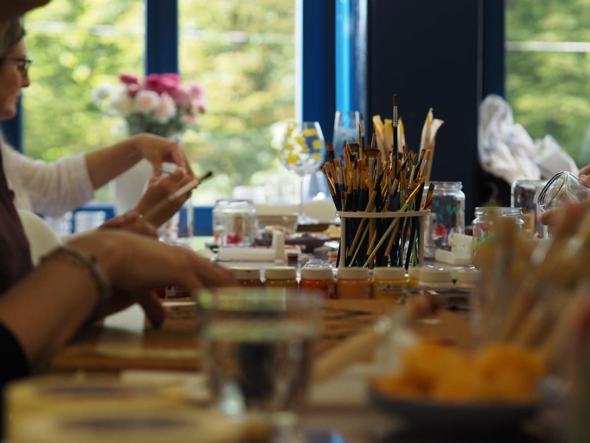 Participants painting together at the long table by the studio windows.
